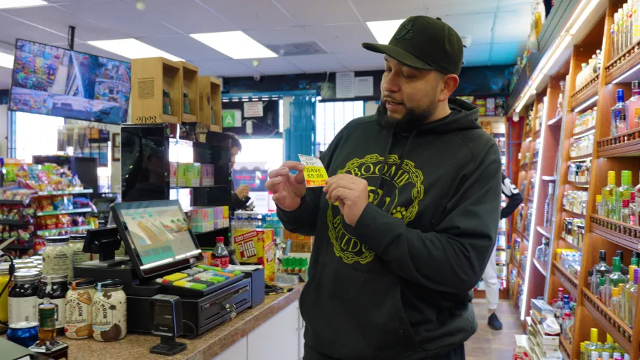 The owner of Michael’s Liquor & Market holding a printed deal tag